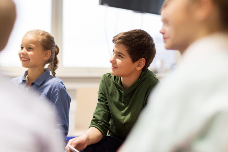 Leerkracht in gesprek met leerlingen in de klas tijdens een kringactiviteit, gericht op groepssfeer met positieve groepsdynamiek