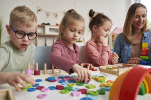 Leerkracht begeleidt kleuters bij taal- en rekenactiviteit in kleine groep.