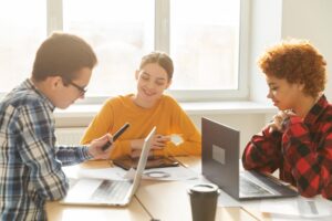 Drie onderwijsprofessionals in gesprek aan tafel met laptop en documenten, werkend aan schoolontwikkeling en kwaliteitsverbetering.
