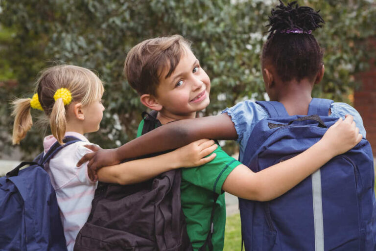 Drie basisschoolkinderen die elkaar omarmen, als symbool voor verbondenheid en samen leren op school.