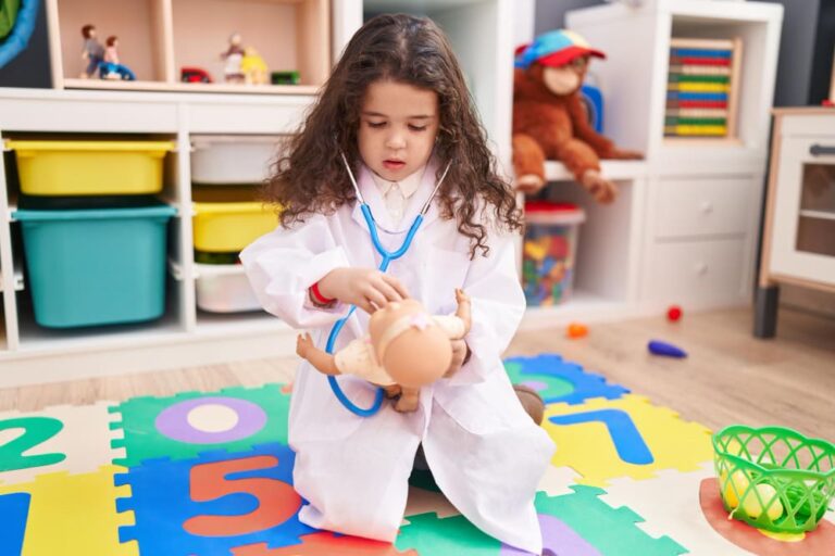 Kleuter in doktersoutfit verzorgt een pop tijdens thematisch spel in de klas.
