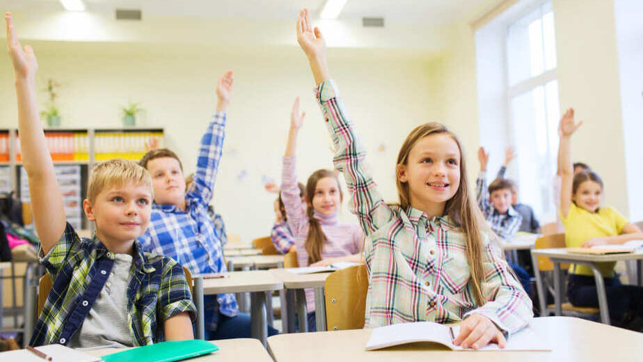 Rustige klas met leerlingen die aandachtig en betrokken meedoen, handen omhoog in een gecontroleerde leeromgeving, leerkracht heeft grip op de klas.