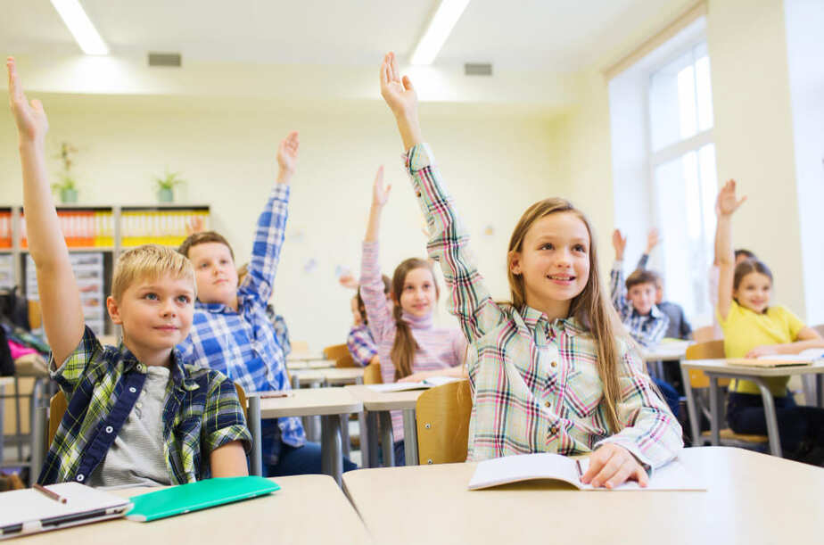 Rustige klas met leerlingen die aandachtig en betrokken meedoen, handen omhoog in een gecontroleerde leeromgeving, leerkracht heeft grip op de klas.