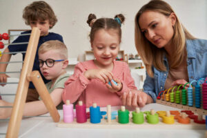 Leerkracht begeleidt kleuters bij spelend leren met educatief materiaal in een ontwikkelingsgerichte klas.