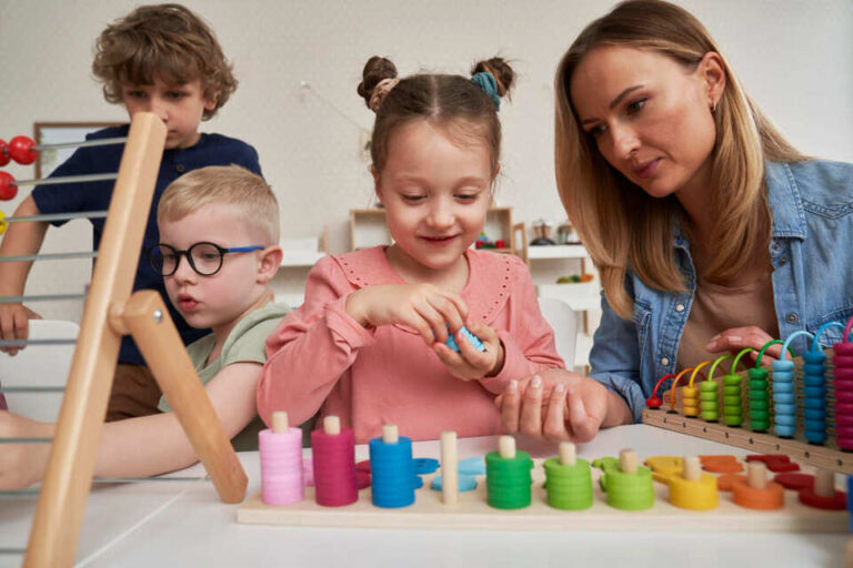 Leerkracht begeleidt kleuters bij spelend leren met educatief materiaal in een ontwikkelingsgerichte klas.