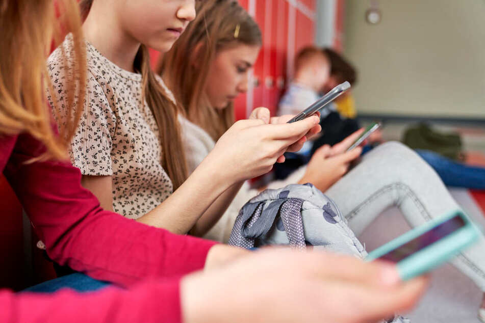 Leerlingen zitten tegen kluisjes op hun telefoon tijdens de pauze.
